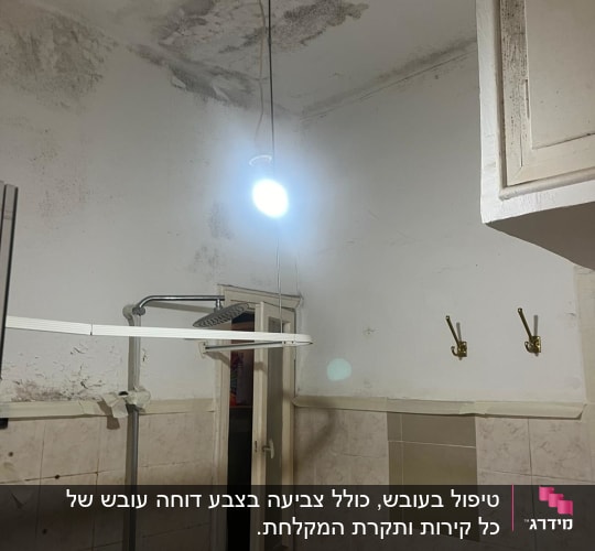 חדר אמבטיה עם עובש בתקרה, חלון פתוח ומנורה תלויה